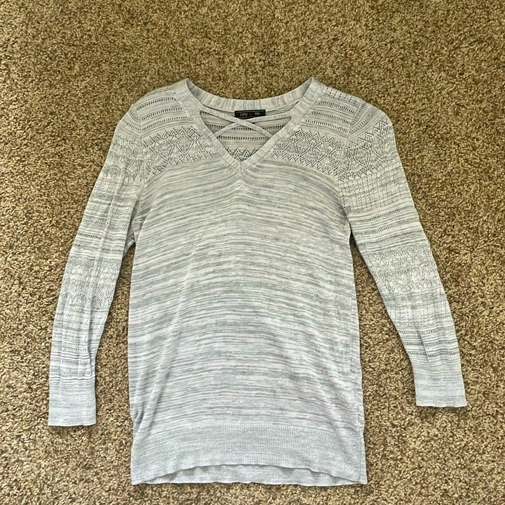 this is a grey sweater with different textures and a cross in the front.